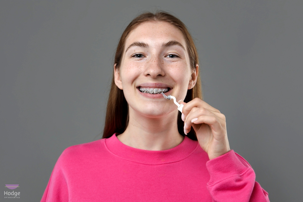 smiling girl metal braces cleaning teeth interdental brush grey background - How to Floss with Braces in Little Rock, AR