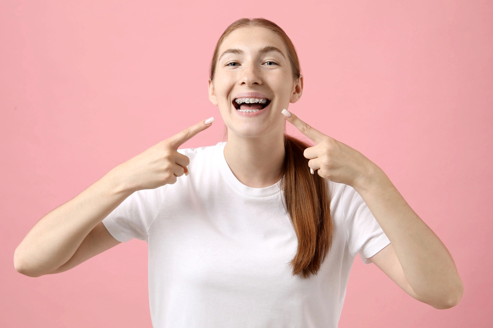 girl pointing her metal braces pink background - How Long Do Braces Take in Little Rock, AR