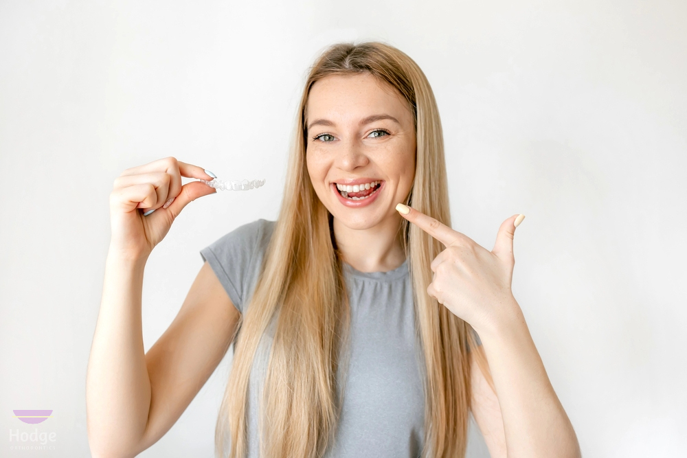 a woman pointing her teeth holding clear aligners - How Does Invisalign Work in Little Rock, AR 