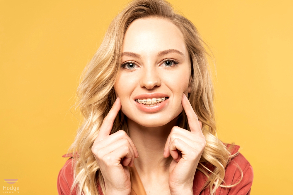 smiling blonde woman clear braces looking camera isolated yellow - How to Clean Braces in Little Rock, AR 